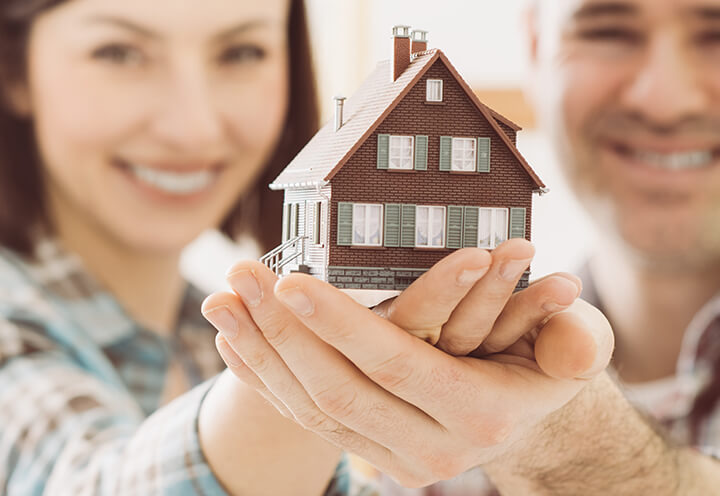Young smiling couple holding up the model of a house | Homeowners Insurance